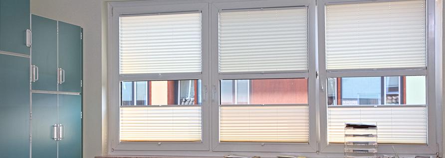 Sechs weiße Plissees an der Fensterfront